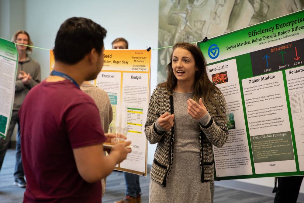 A student speaks to a guest about her poster presentation